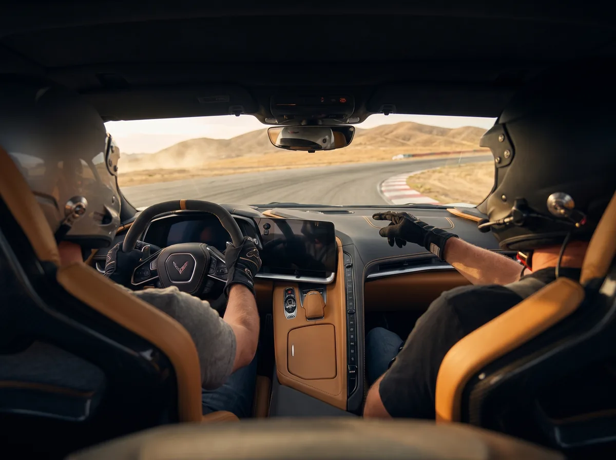 Inside a sports car on track, a coach in the passenger seat points through the windshield at the next corner
